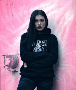 Person in black hoodie, pink background.